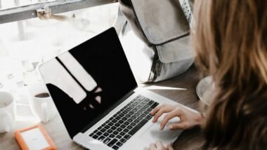 girl wearing grey long-sleeved shirt using MacBook Pro on brown wooden table